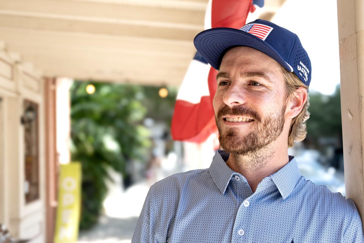 A man wearing an American flag hat branded with downtown Bastrop logo (event giveaway)
