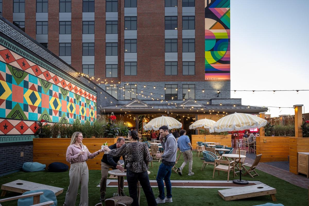 People enjoying beverages outside of a colorful mural at Bar Kapu