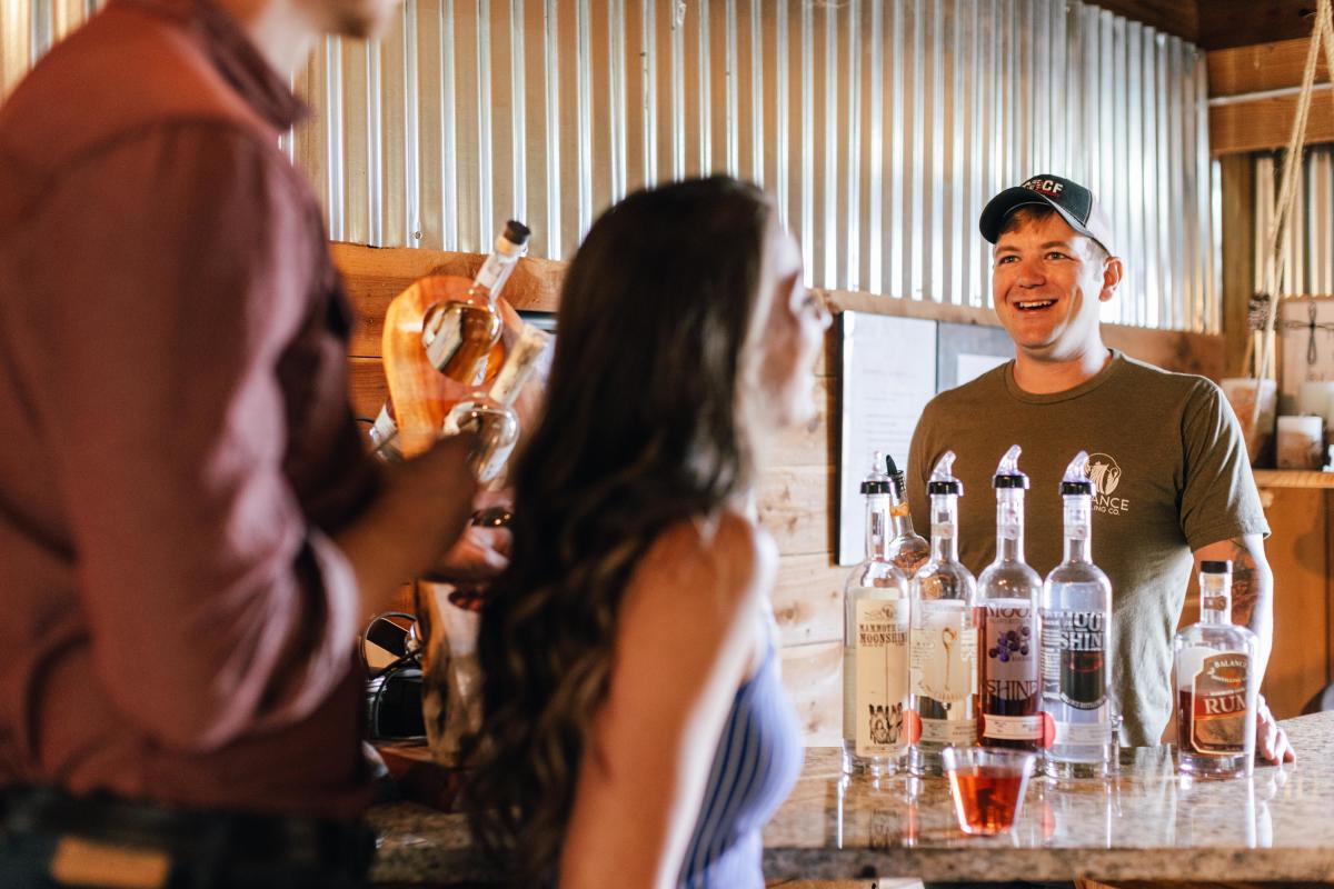 Picture of a couple enjoying drinks while speaking to the owner of the distillery they are at, at Balance Distilling Company