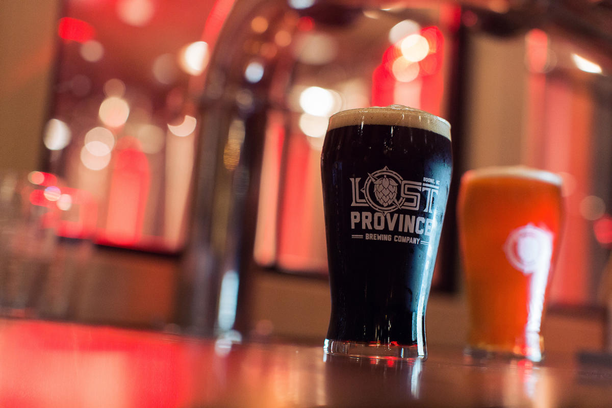 Two full beer pints sit atop a bar. The glasses have been etched with the Lost Province Brewing Company logo.