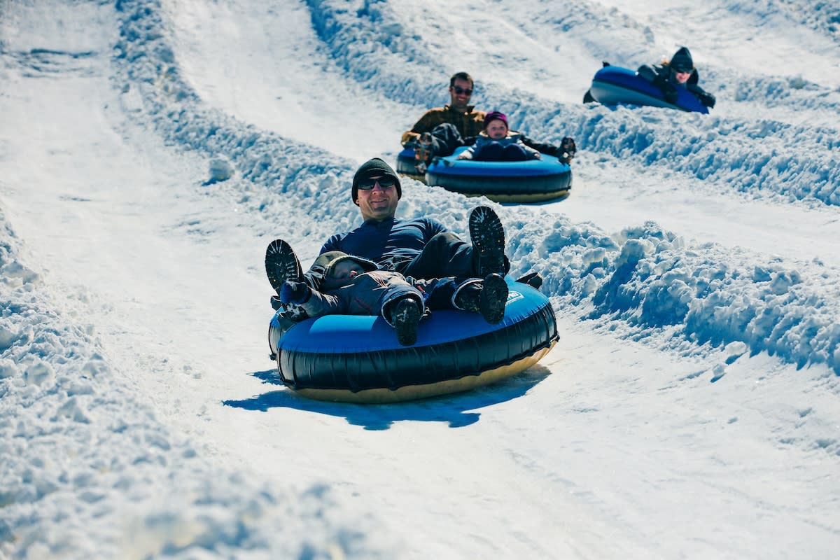 Snow tubers smile as they descend a snowy hill in different lanes.