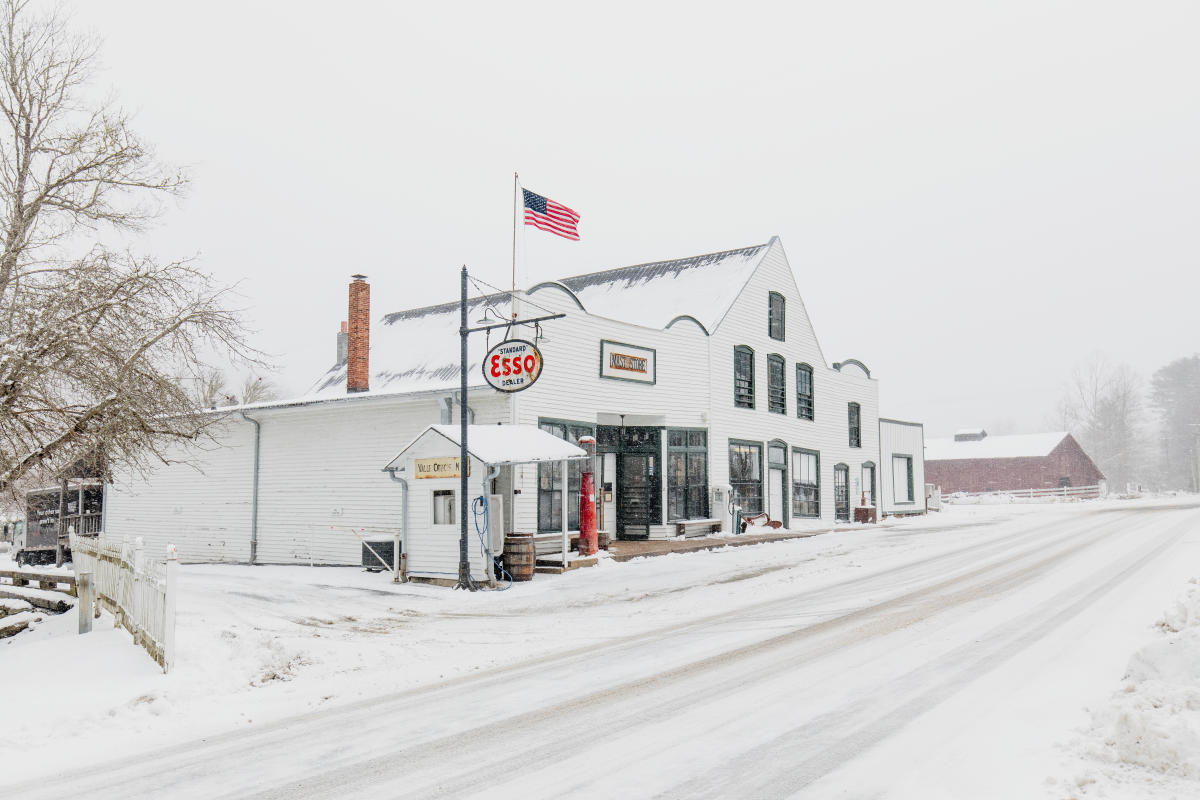 The original Mast General Store in Valle Crucis is blanketed in snow. Old signage and the American flag a bright against a white backdrop.