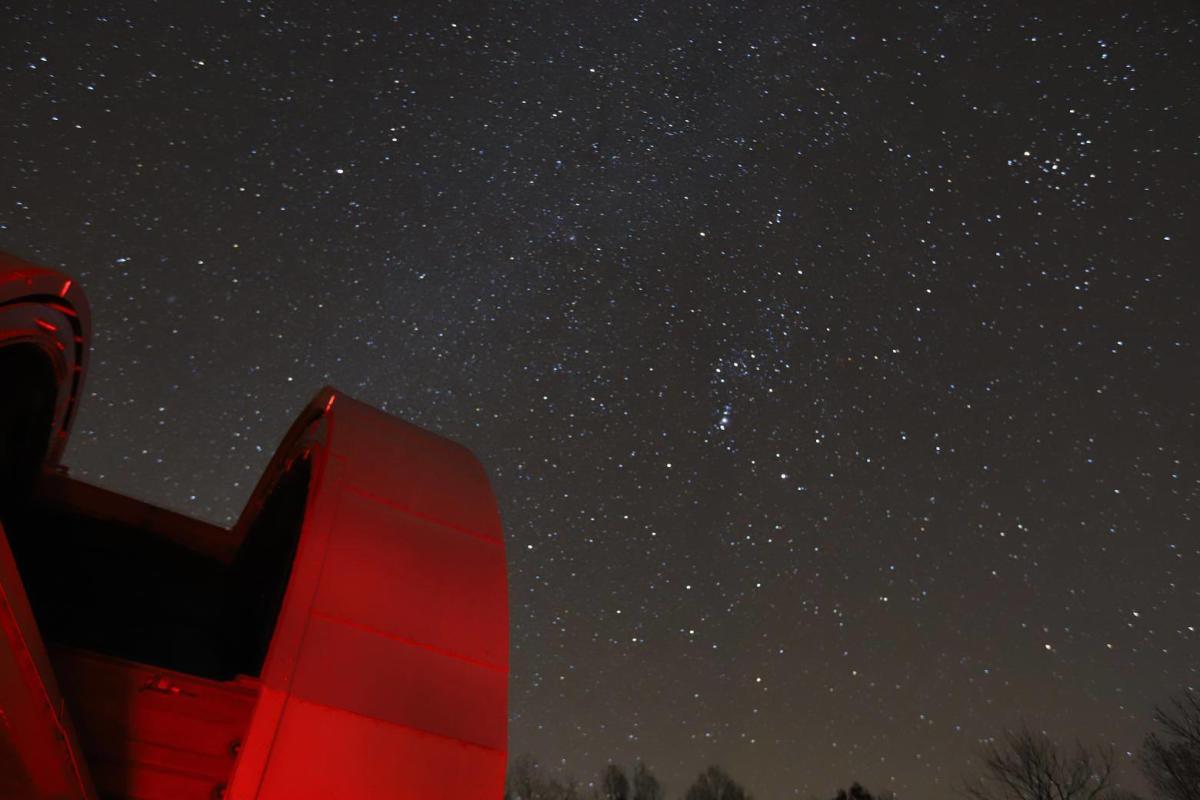 A vast night sky filled with stars. The red-tinted edge of a large observational telescope can be seen in the lower left corner.
