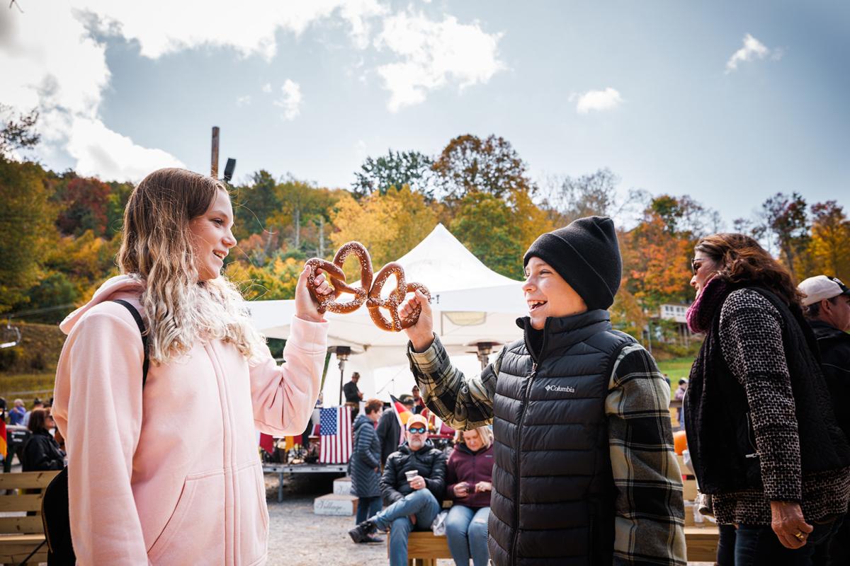 Two children laugh as they both hold twisted, salted pretzels at a fall festival.