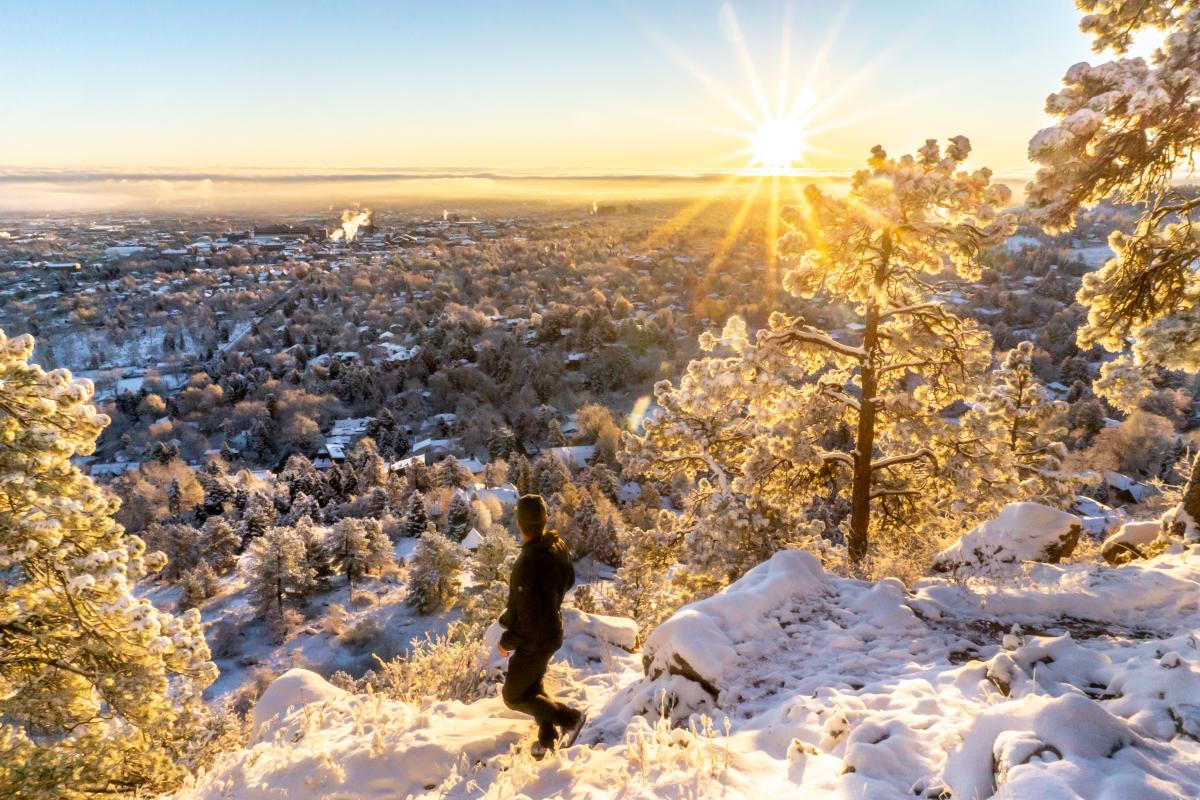 A person looking out at a spectacular view of Boulder as the sun rises while on a winter hike.