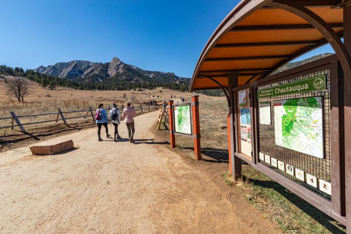 A group of three hiking at Chautauqua Park Trailhead with the Flatirons in view