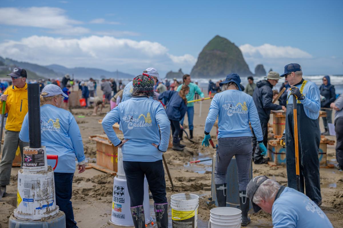 A team gathers on the beach as they work together to build a sandcastle sculputure.