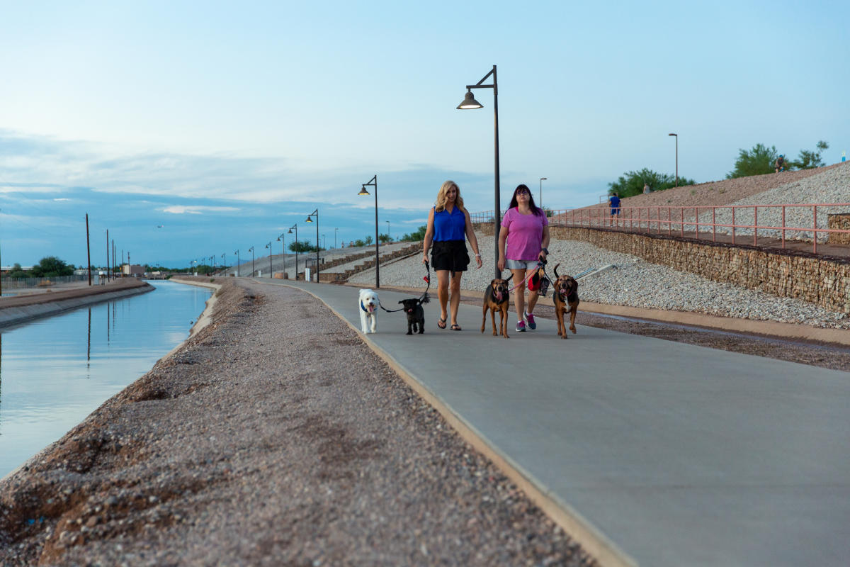 two ladies walking four dog on a paved walkway along a canal in Chandler, az