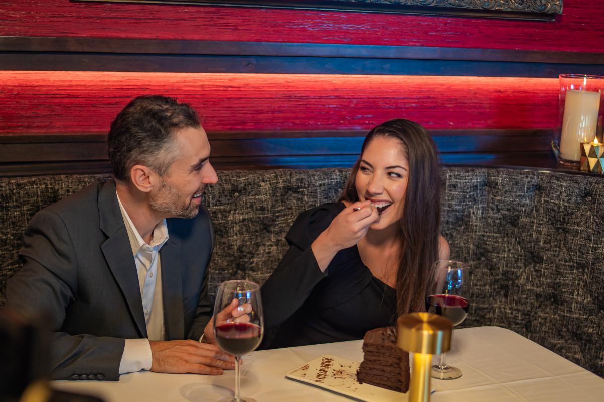 a couple enjoying a glass of red wine and a slice of chocolate cake while sitting in a restaurant booth