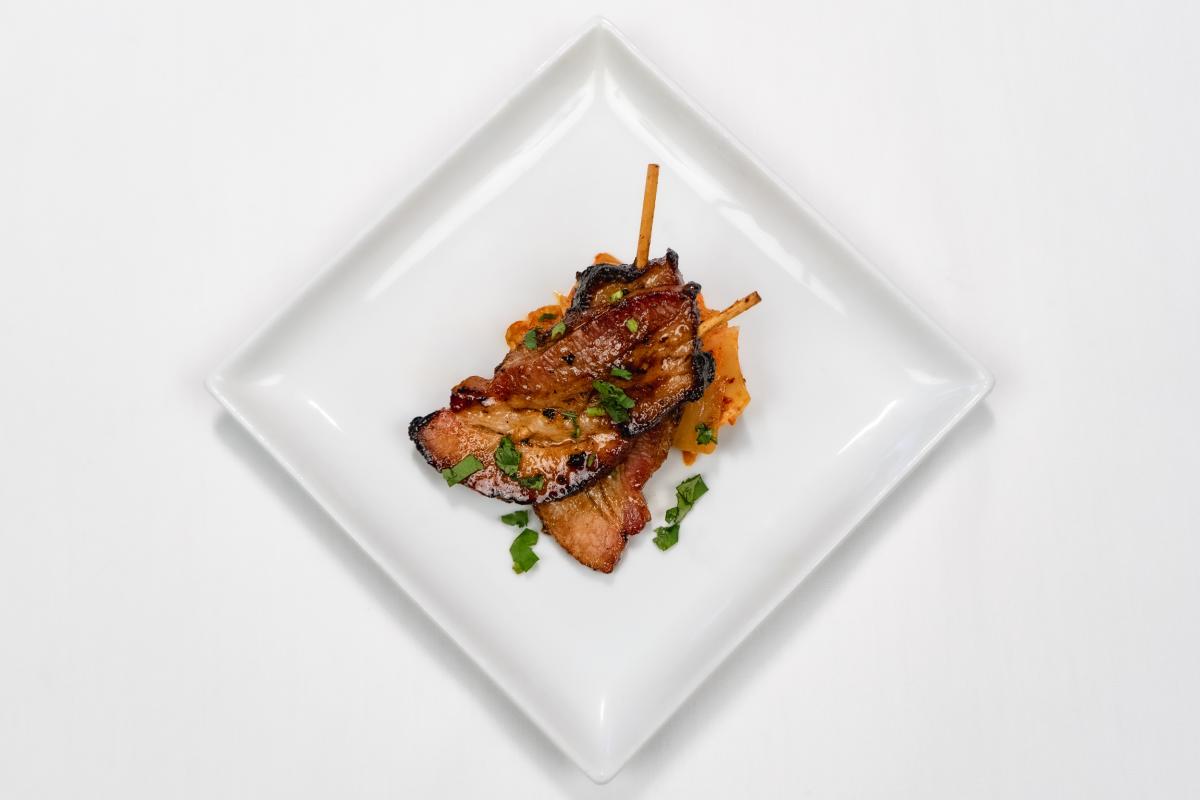 a white square plate with two beef skewers and sauce