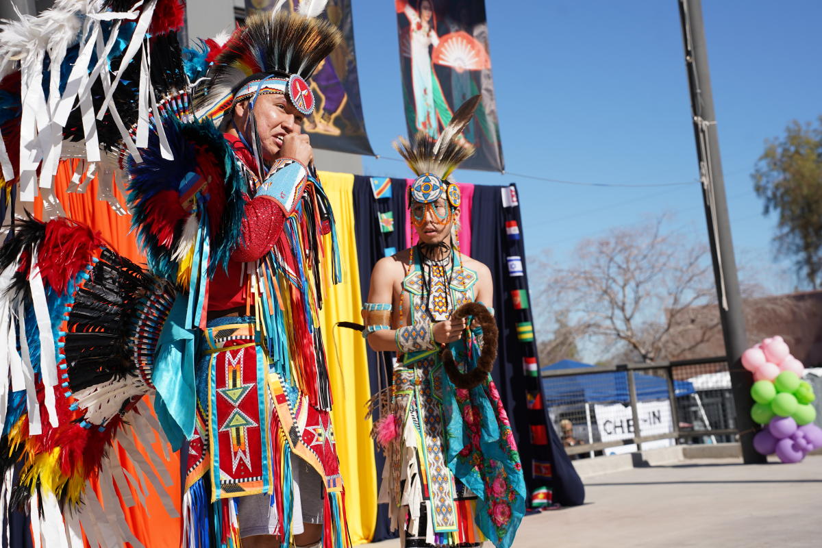 two Native American Dancers perform in traditional dress on an outdoor stage