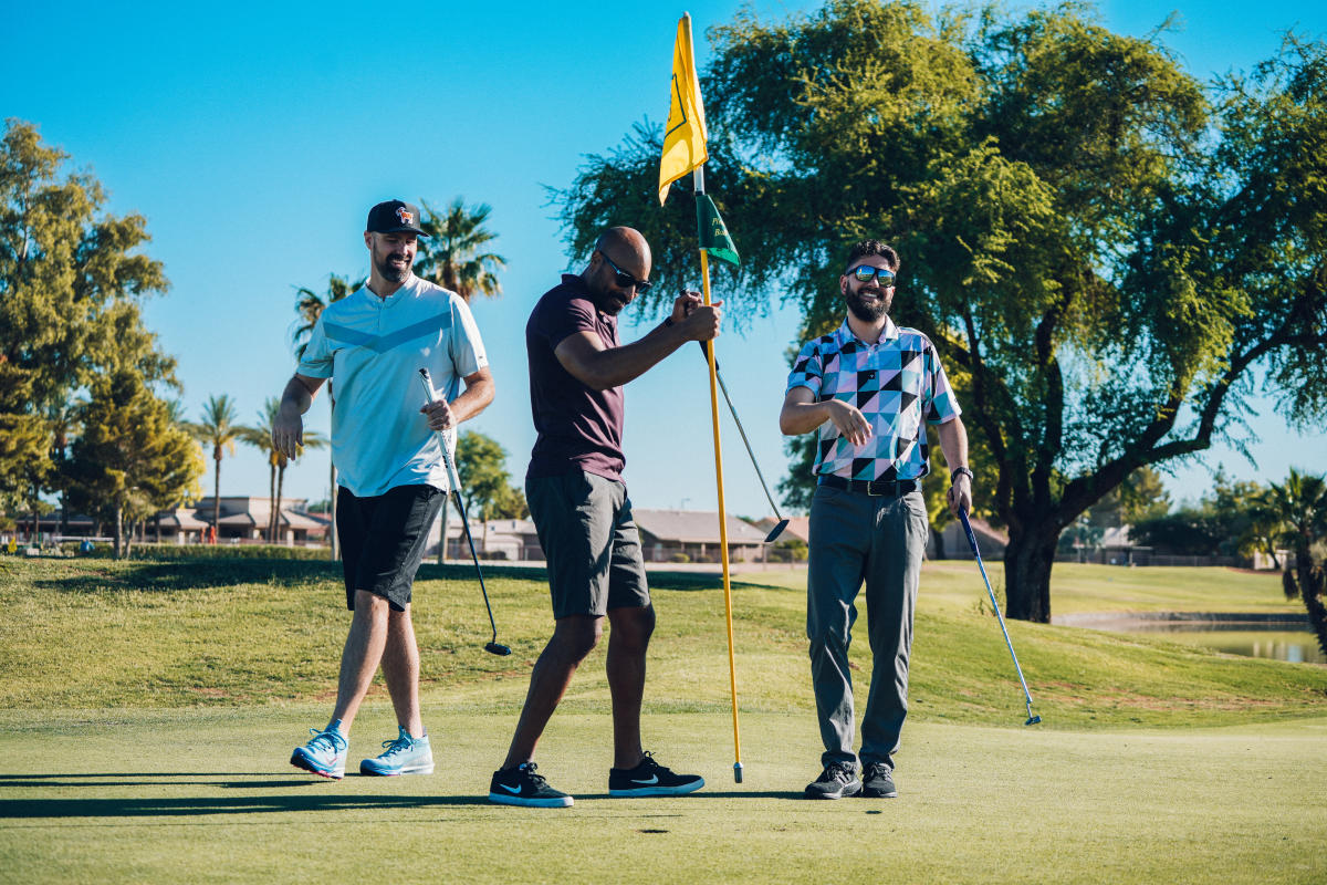 Three men putting and lifting flag during golf round.