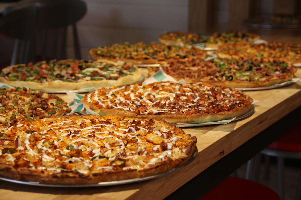 a table filled with six large pizza with various toppings