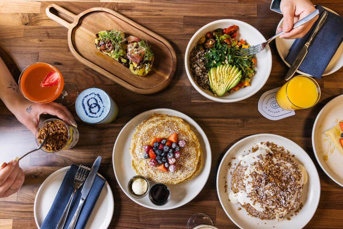 Aerial view of plates with pancakes, avocado toast, salad and drinks on the table.
