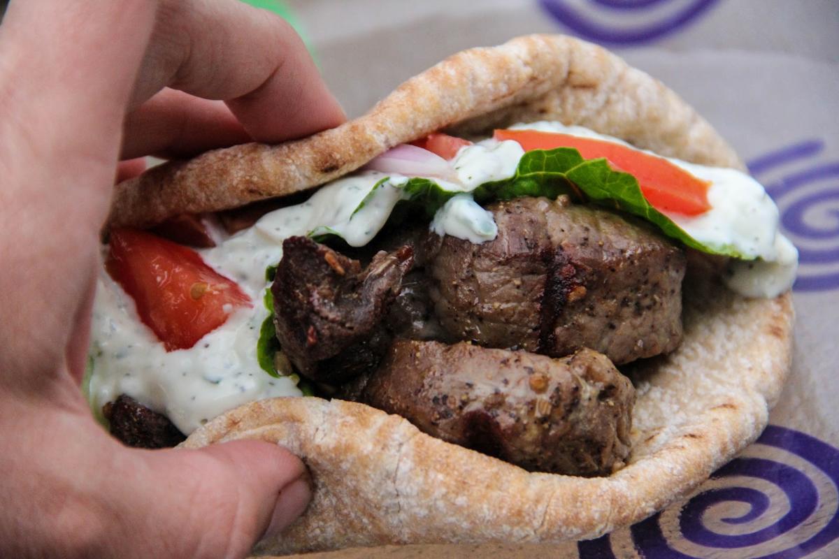 Close-up view of a freshly prepared Greek gyro with succulent slices of grilled meat, ripe tomatoes, crisp lettuce, and creamy tzatziki sauce in a soft pita bread.