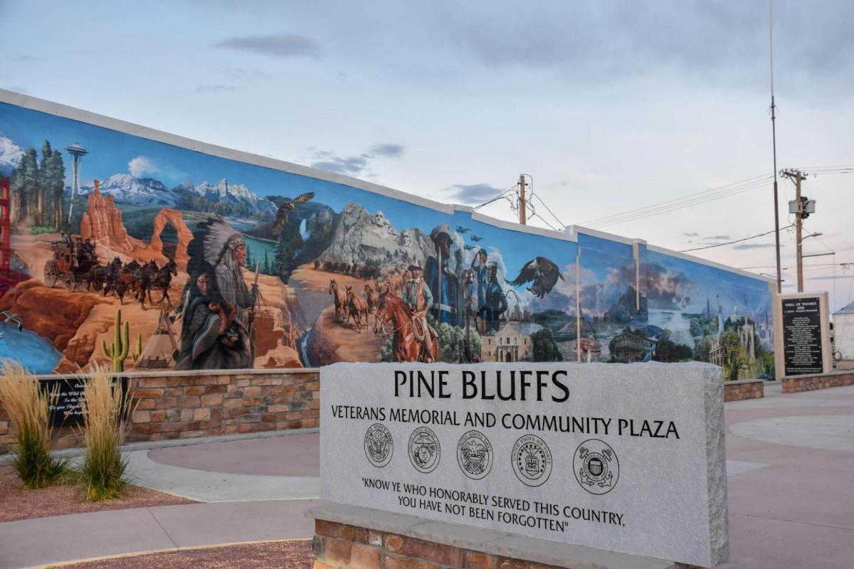 A sign for the Pine Bluffs standing before a mural.