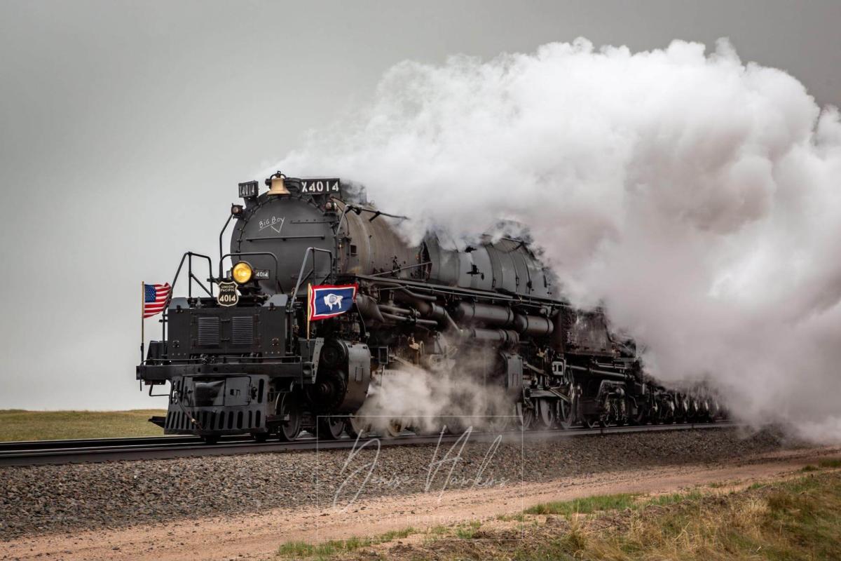 Union Pacific Big Boy 4014 steam locomotive charging through a field with a thick plume of steam, adorned with American and Union Pacific flags.