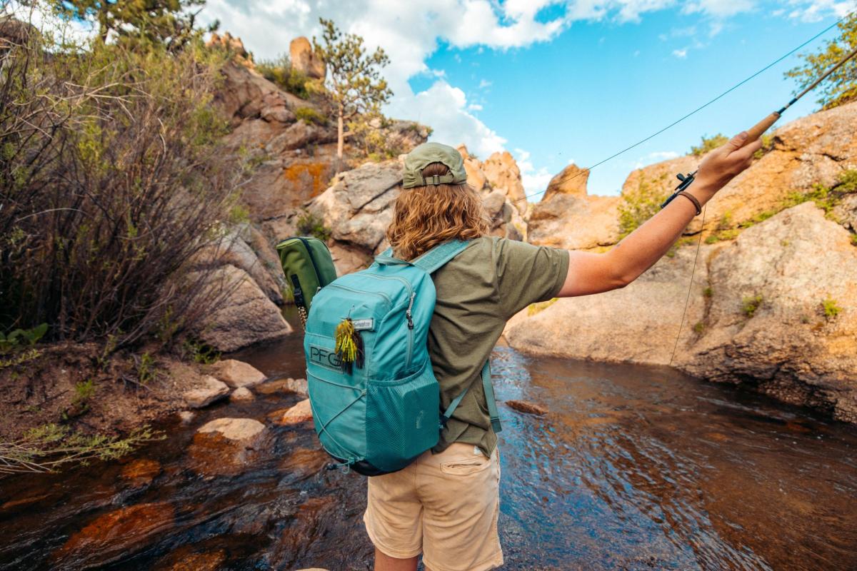 Fly fisher casting line in a rocky Wyoming creek surrounded by rugged nature.