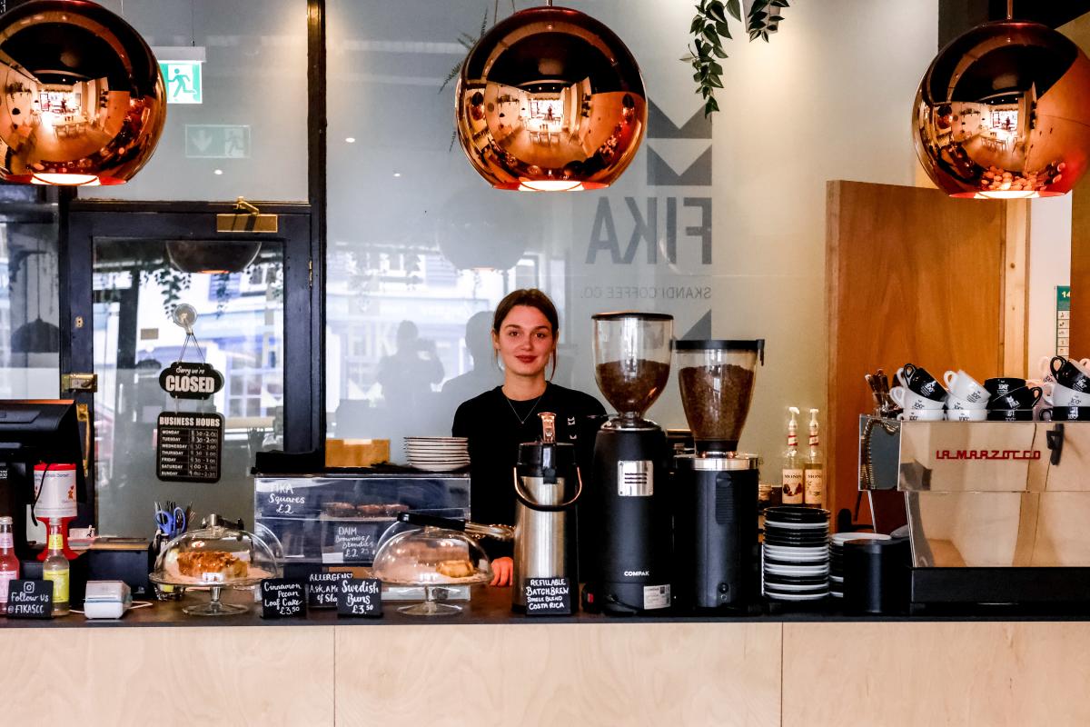 A female barista behind a counter with coffee equipment.