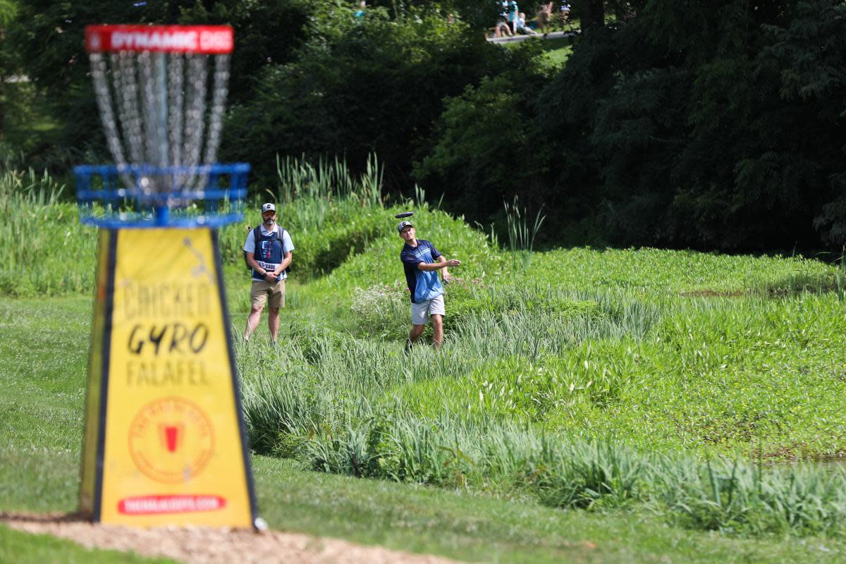Image is of a pro throwing the disc toward a hole.