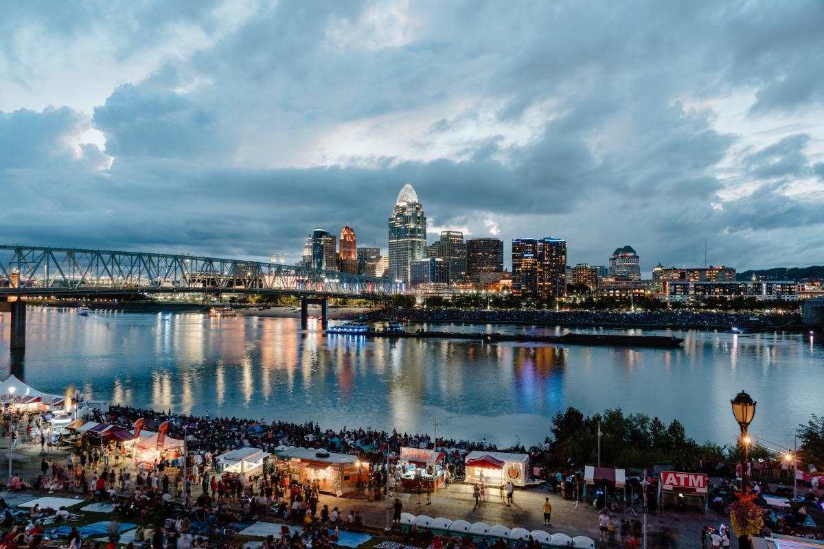 Crowds of people gather along the river as the sun goes down.