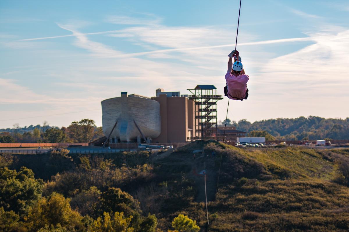 Image is of person zip lining toward the Ark Encounter.
