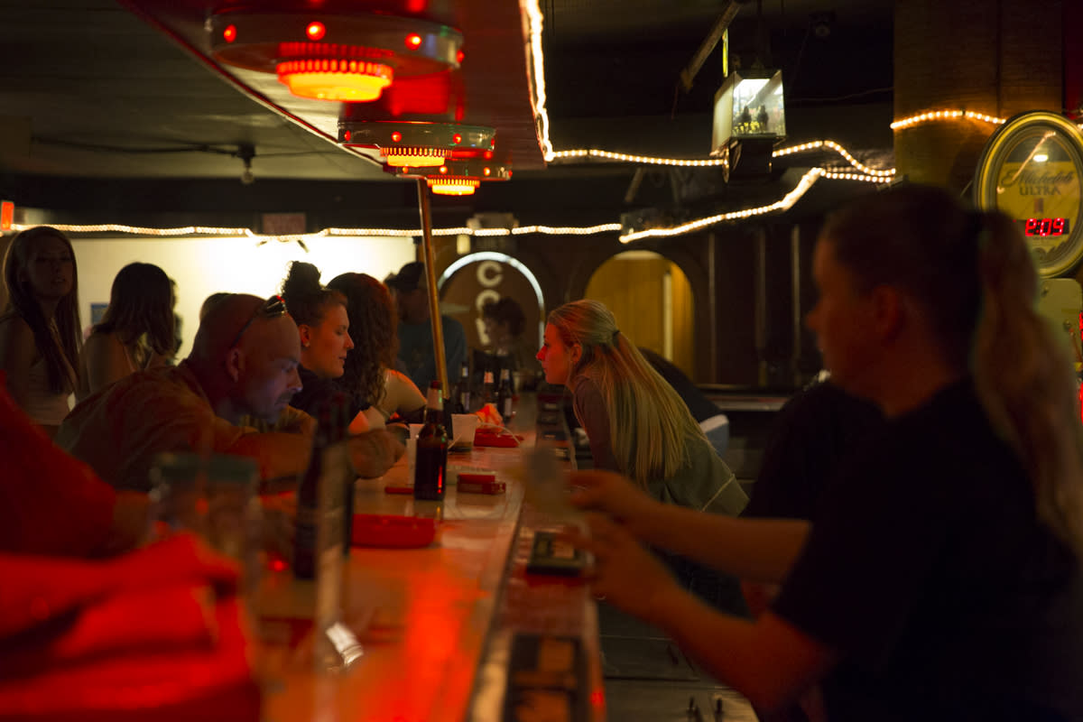 Image is of patrons and bartenders interacting with a bar top in between them.