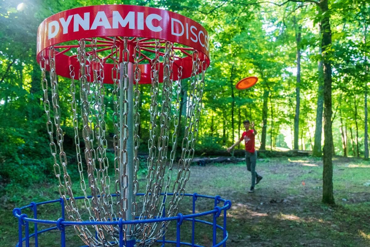 A man throwing a disc to a chain basket at Idlewild Disc Golf course