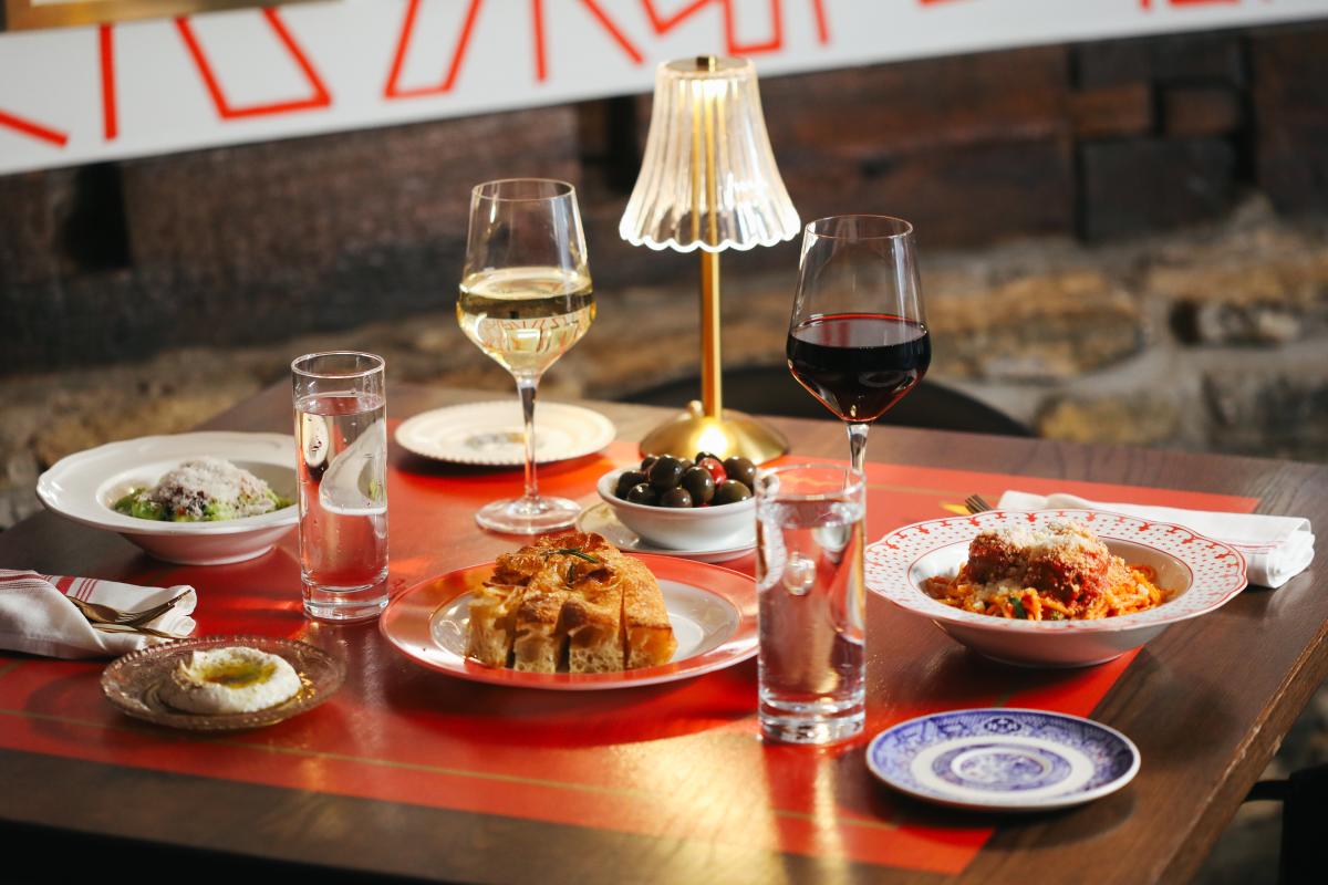 The image is of a table set at Mama's on Main which includes a light, two glasses of wine, two glasses of water, cheese bread, olives, a pasta dish and a salad.