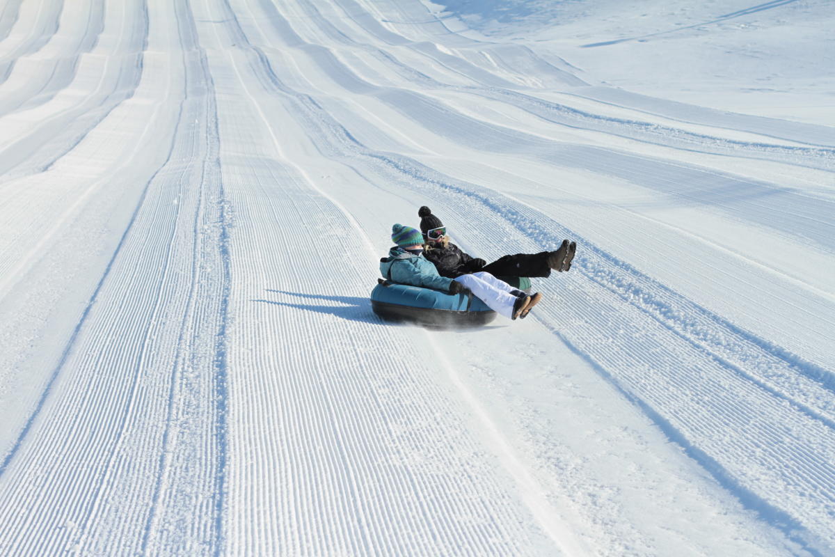 Image is on two people sharing a black inner tube sliding down a hill covered in snow.