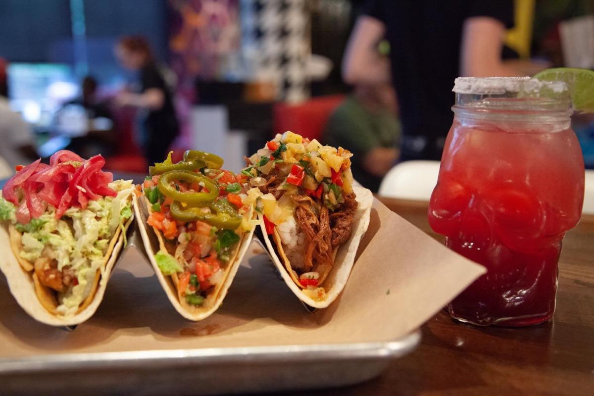 Three tacos held by taco stand with a pink margarita in a skull shaped glass at Agave & Rye in Covington, Ky.