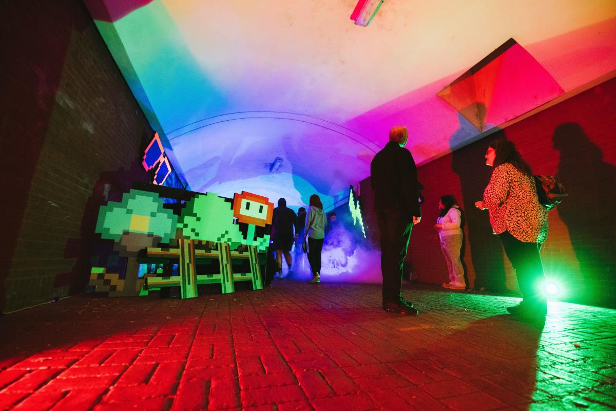 People in a tunnel lighted green, red, blue with 16 bit art for BLINK Cincy