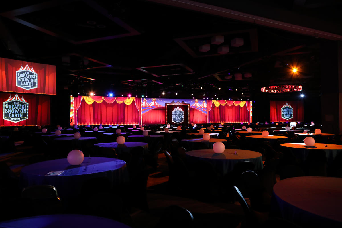 Circus signs reading "The Greatest Snow on Earth" hang from red tapestries with many round tables in the foreground