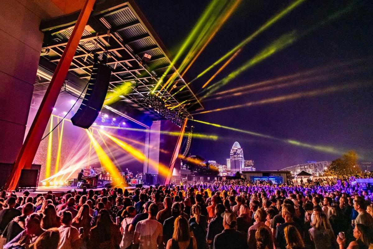 Night concert outdoors with rays of yellow light at Promowest Pavilion in Newport, Ky, with the Cincinnati skyline in the background