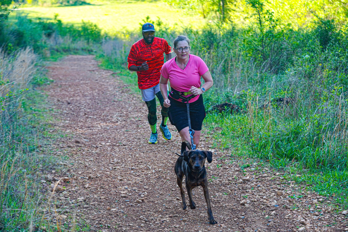 man and woman on a running trail with a dog