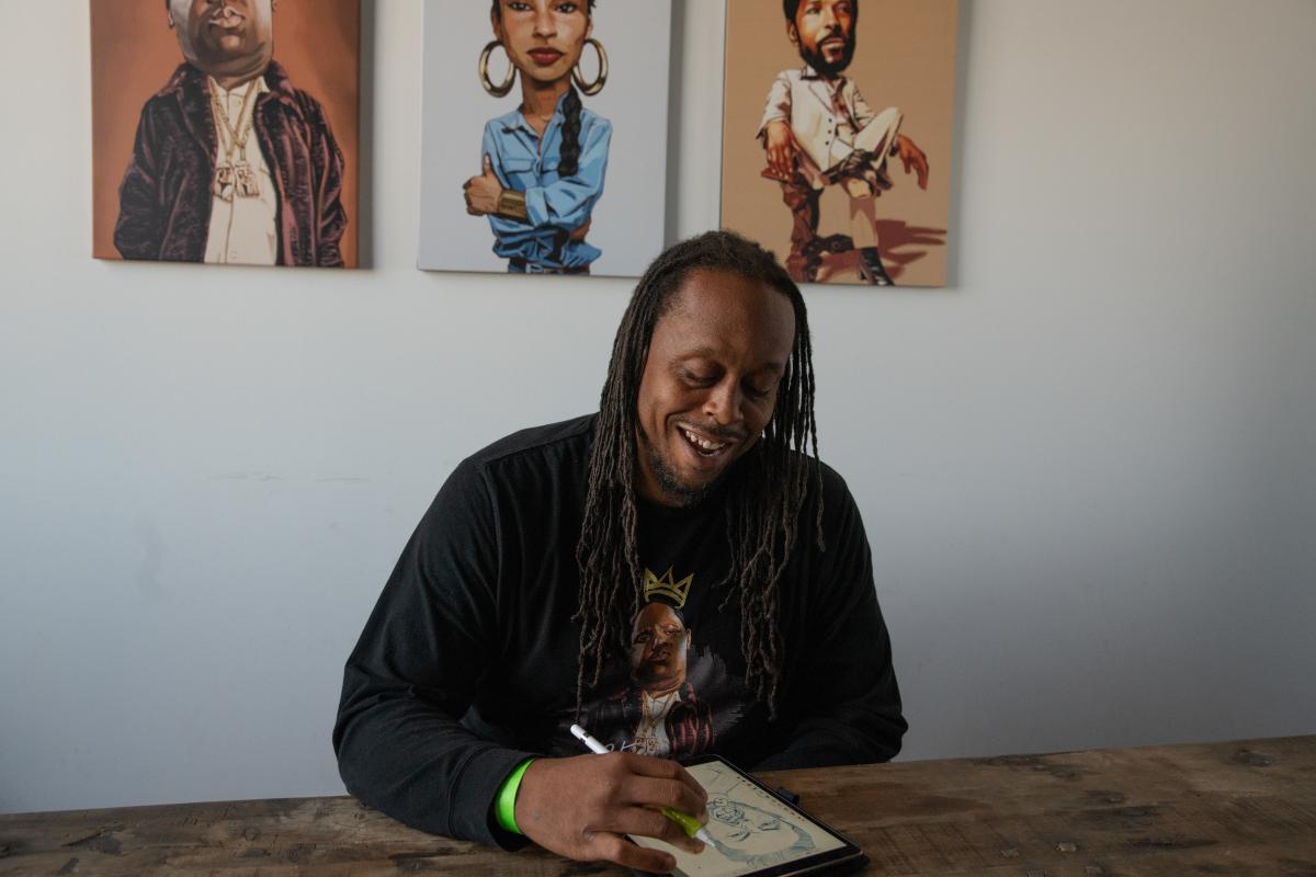 Artist Evan Williams creates digital art, with three of his prints in the background