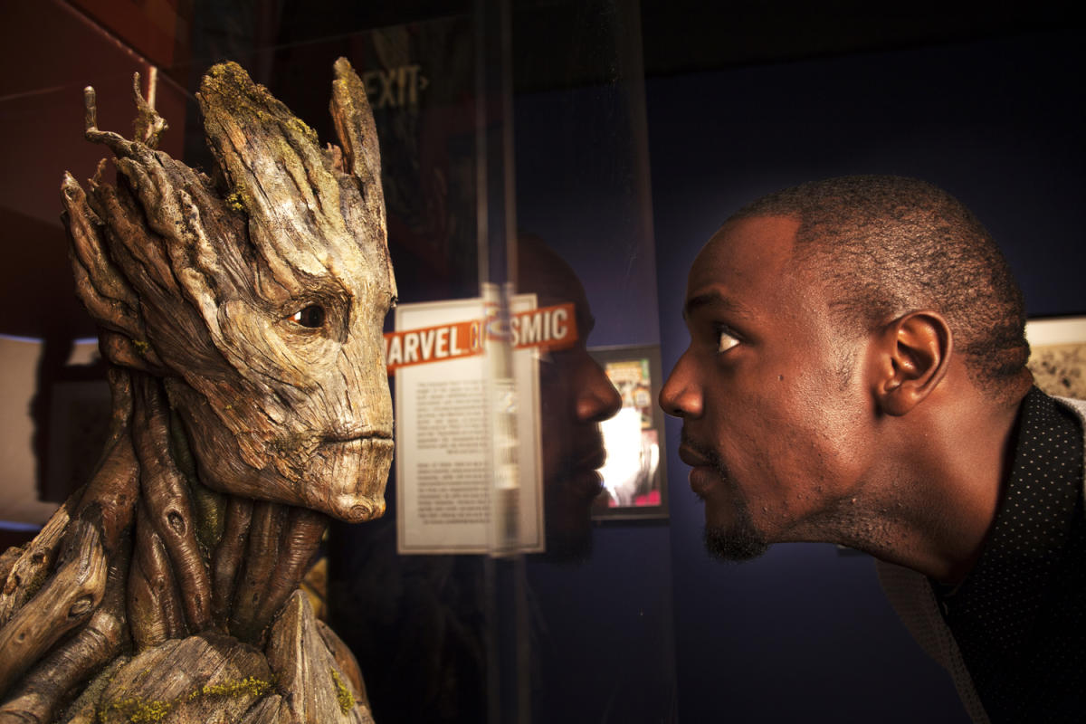 A man leans close to a Groot sculpture at COSI's Marvel exhibit