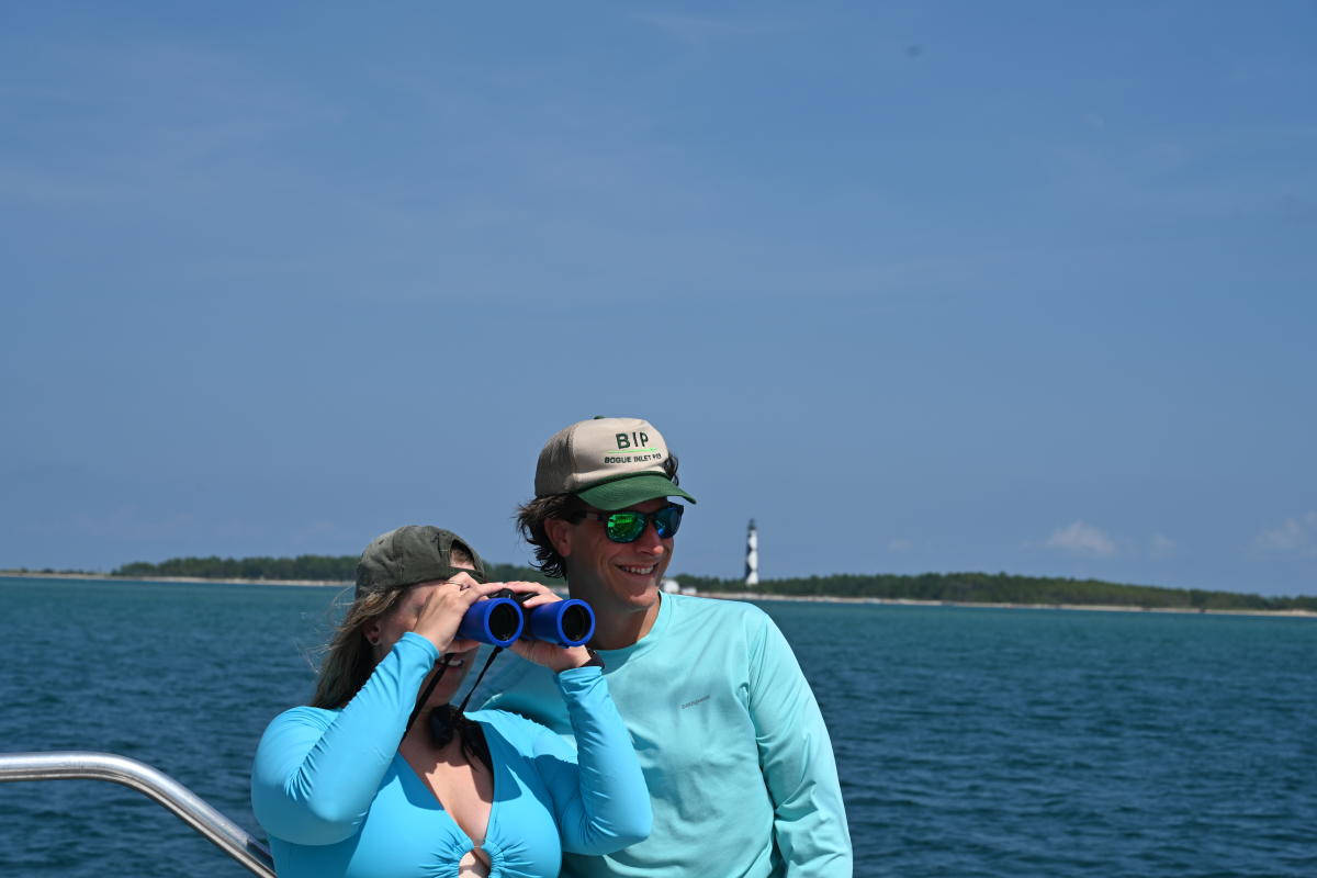 Couple with Lighthouse Behind them Looking through Binoculars