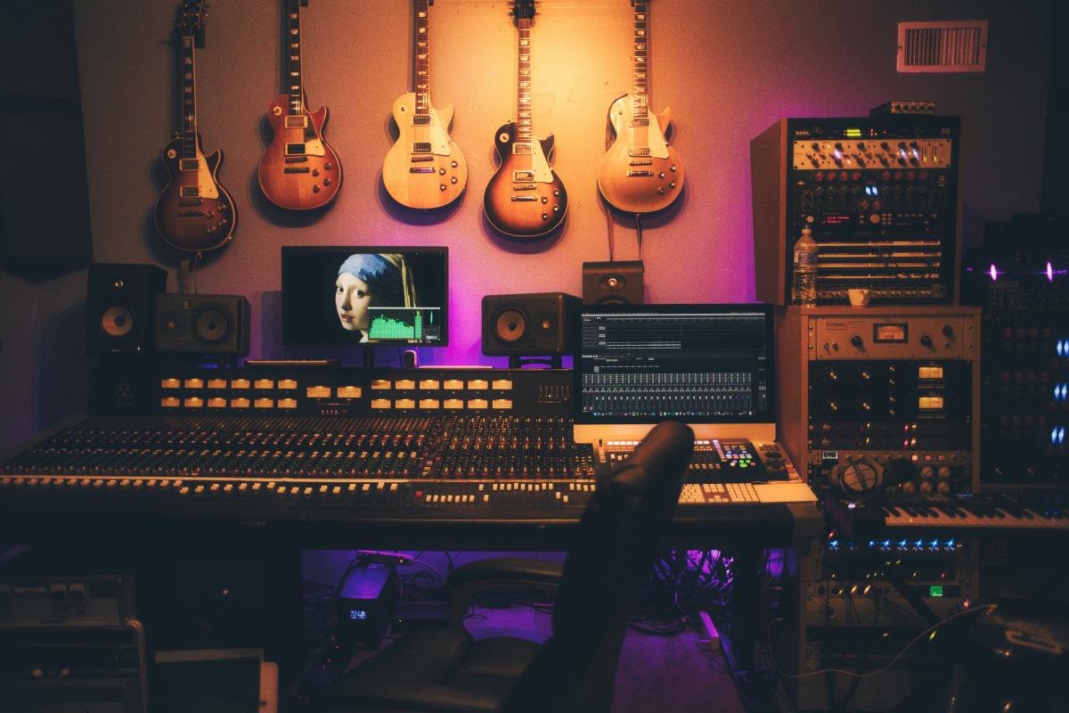 Inside of a recording studio with equipment set up across the wall with guitars hanging on the wall