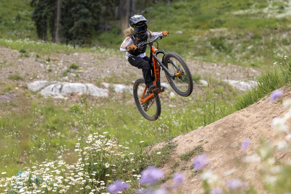 A kid doing a mountain bike jump in a field of flowers at Purgatory Resort.