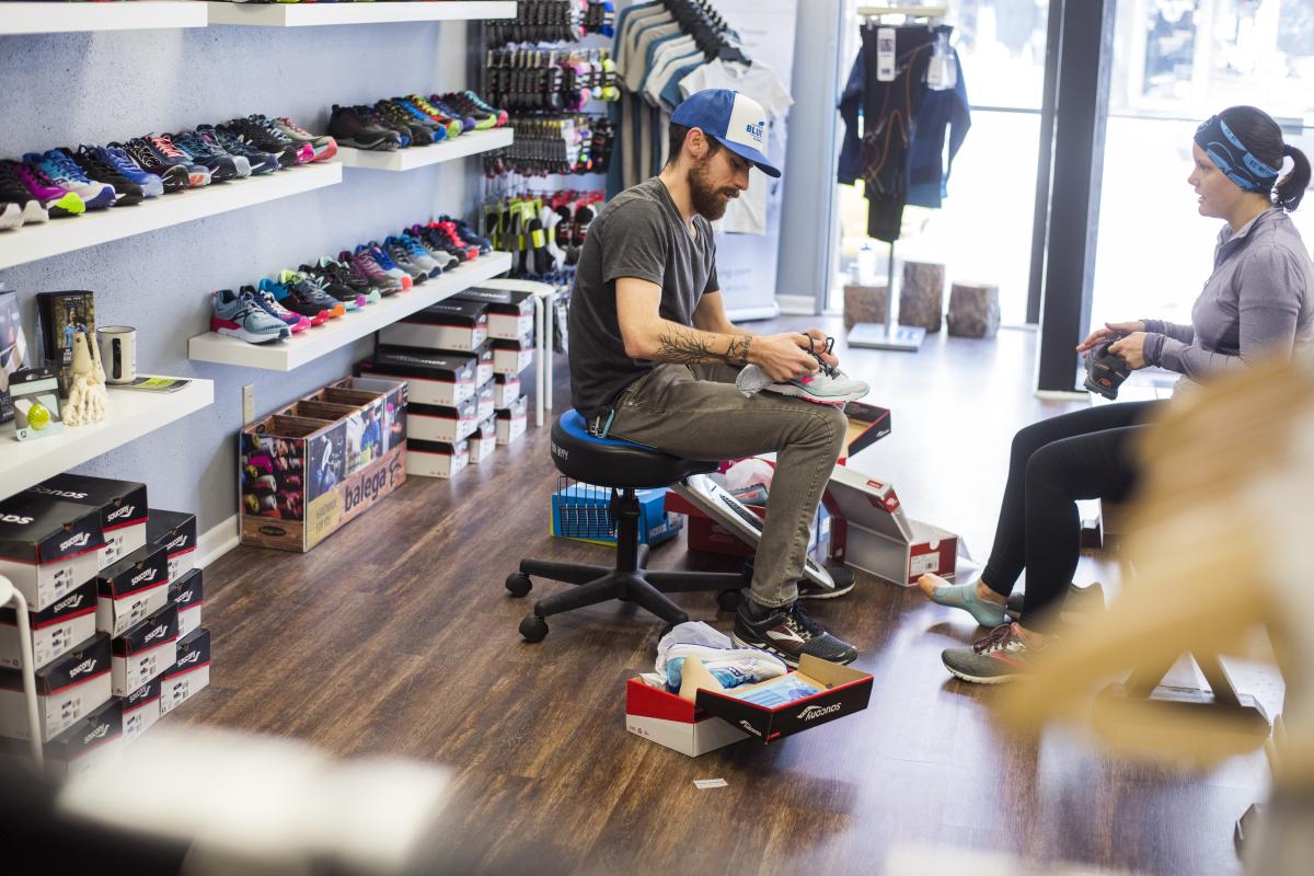 Store clerk helping a woman try on shoes at Blue Ox Running Store