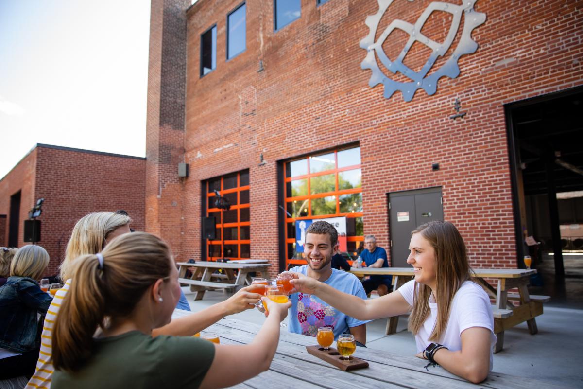 A group of four friends cheers their drinks on the outdoor patio at The Brewing Projekt in downtown Eau Claire