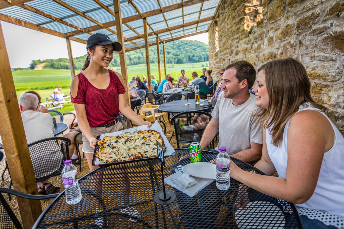 A couple dining outside and a server delivering pizza