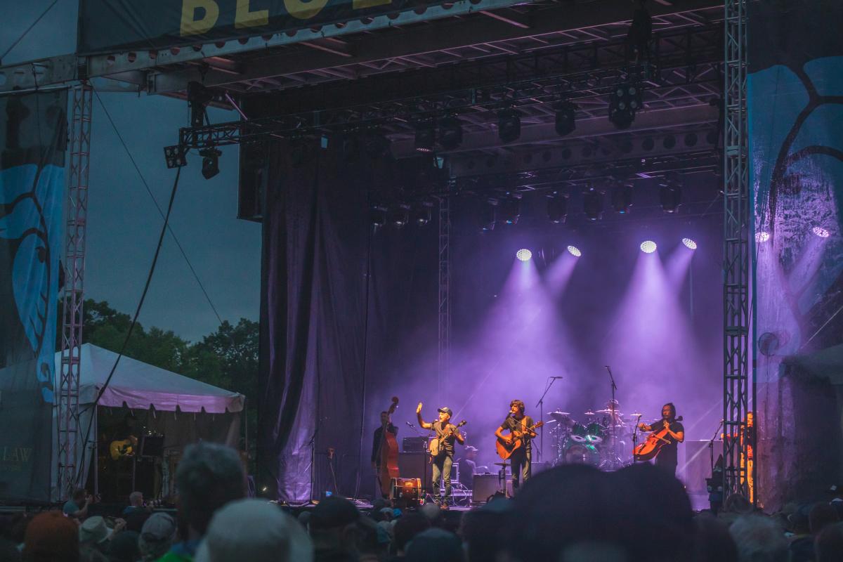 A band on stage performing at dark with purple lights at Blue Ox Music Festival