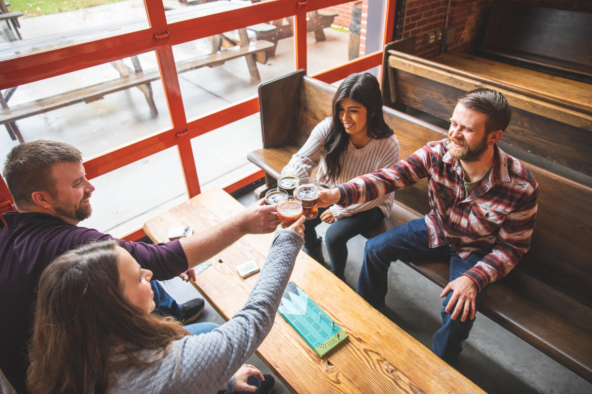 A group of 4 friends cheers their beer and play cribbage at the Brewing Projekt