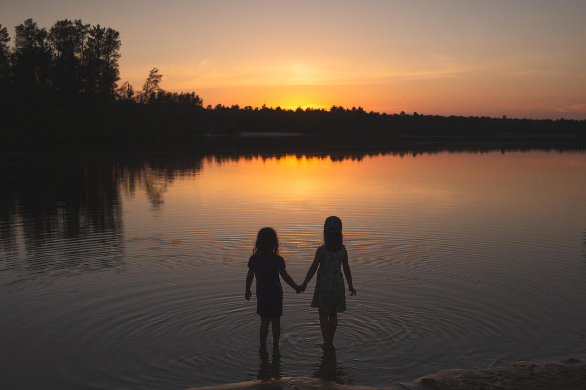 Two girls holding hands in the water at sunset at Coon Fork Lake County Park