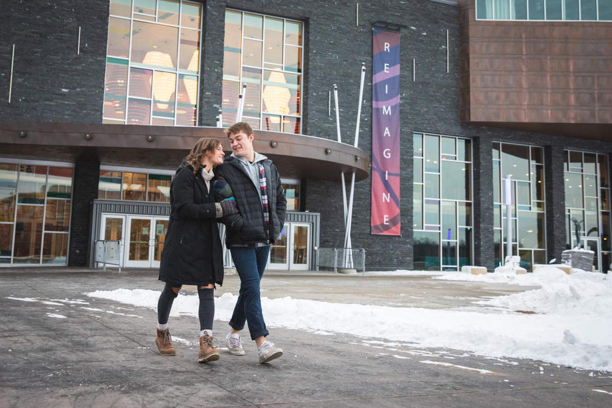 A couple, male and female, walking hand in hand in front of the Pablo Center in the winter