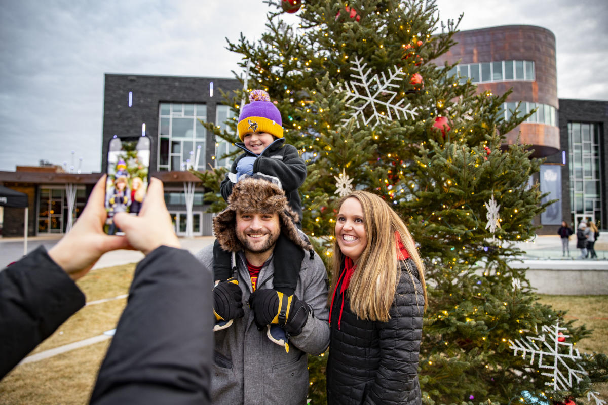 A family posing for a photo in front of a holiday tree at Haymarket Plaza during Wintertime in the City