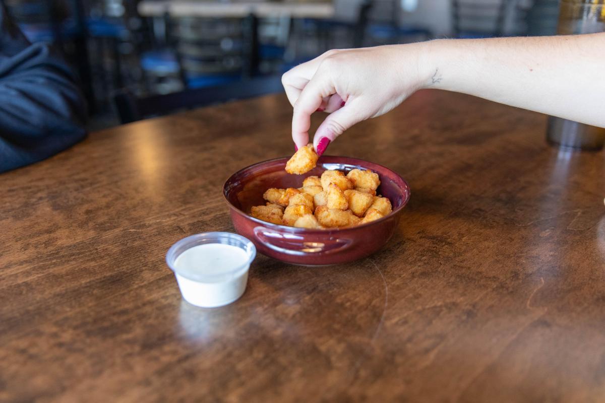 A hand dipping a cheese curd into ranch at Fella's Loaded Goat