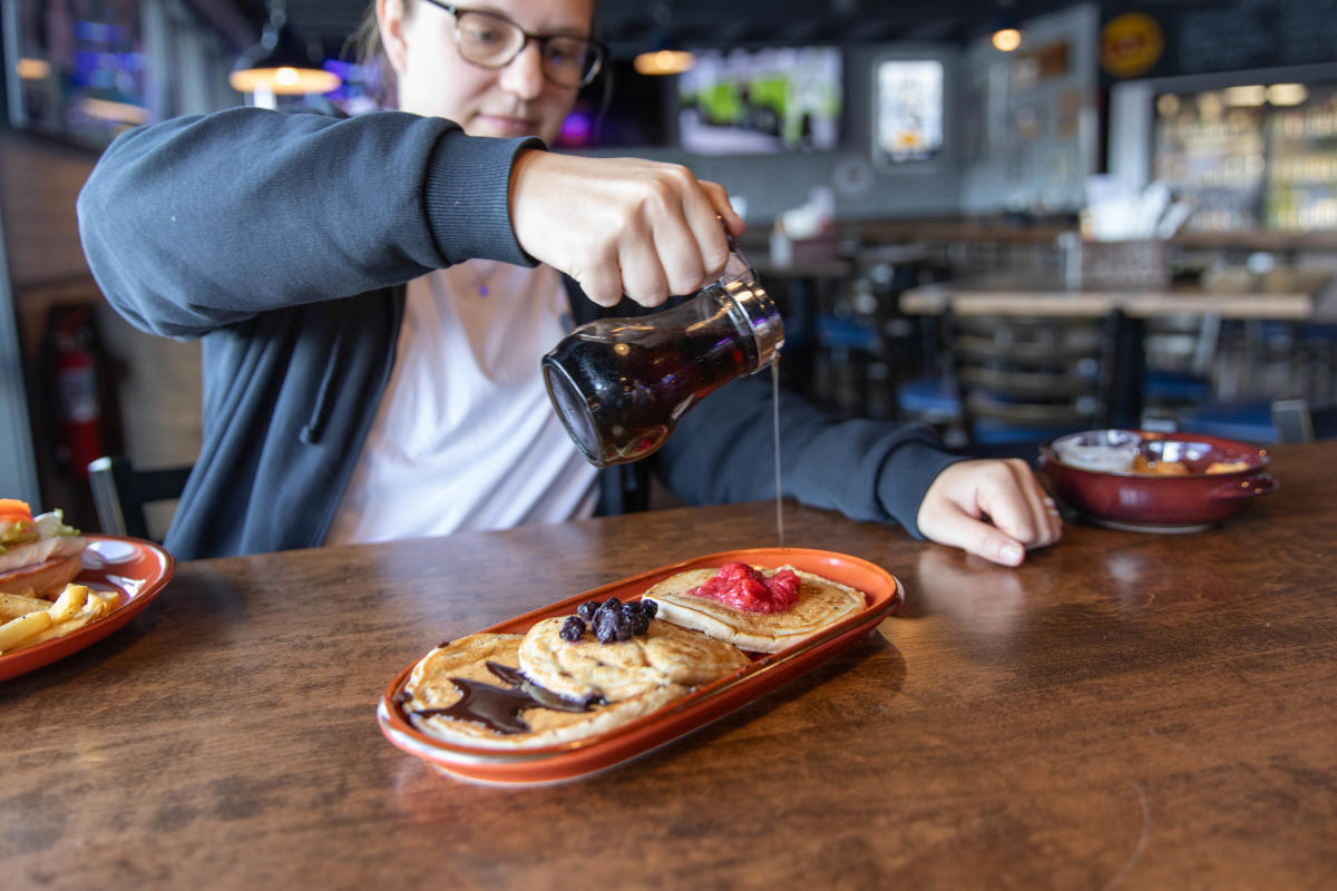 A girl pouring syrup over her pancake flight at Fella's Loaded Goat